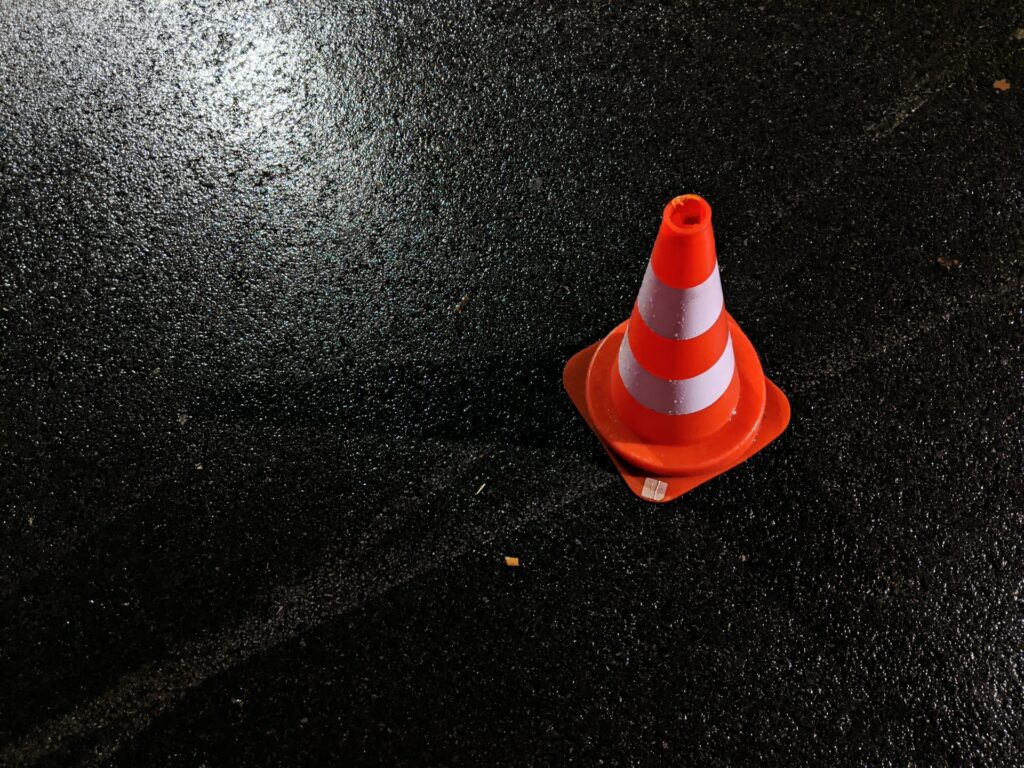 Ein Verkehrsleitkegel auf dunklem Asphalt.